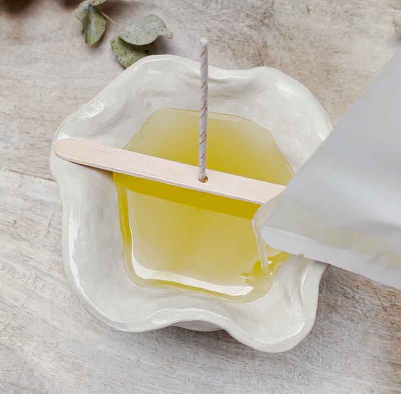 Pouring melted wax into a handmade ceramic candle mold with a centered wick using Sculpd Candle Making Kit