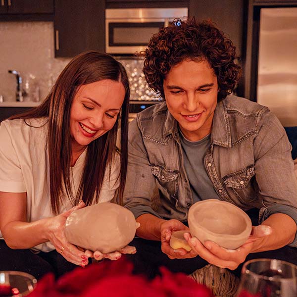 Two unpainted Sculpd Pottery Kit clay pots held aloft by two people