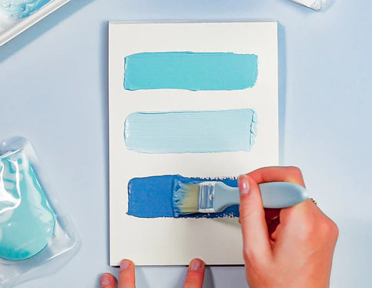 A person using a brush to paint a small canvas with abstract shapes painted in shades of blue using Sculpd Canvas Painting Kit