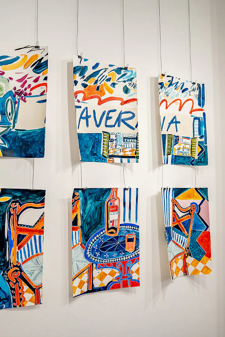 Vibrant, hand-painted artworks featuring Mediterranean-inspired scenes, hung against a wall with suspended wires made with Sculpd Canvas Painting Kit 