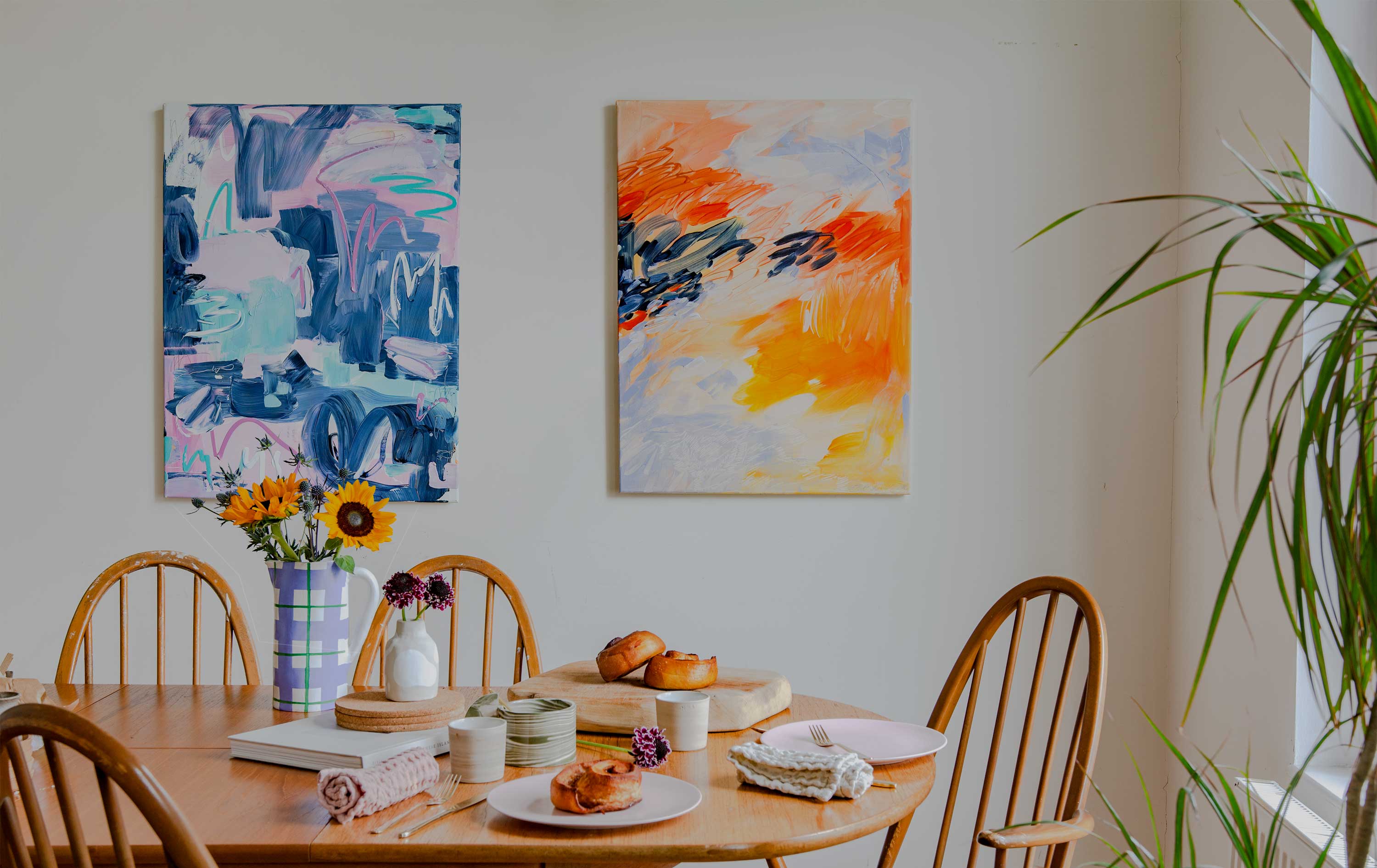 Abstract Paintings made using Sculpd Canvas Painting Kit displayed on a wall with a kitchen table artfully displaying  bread, flowers, plates and dining utensils on the foreground