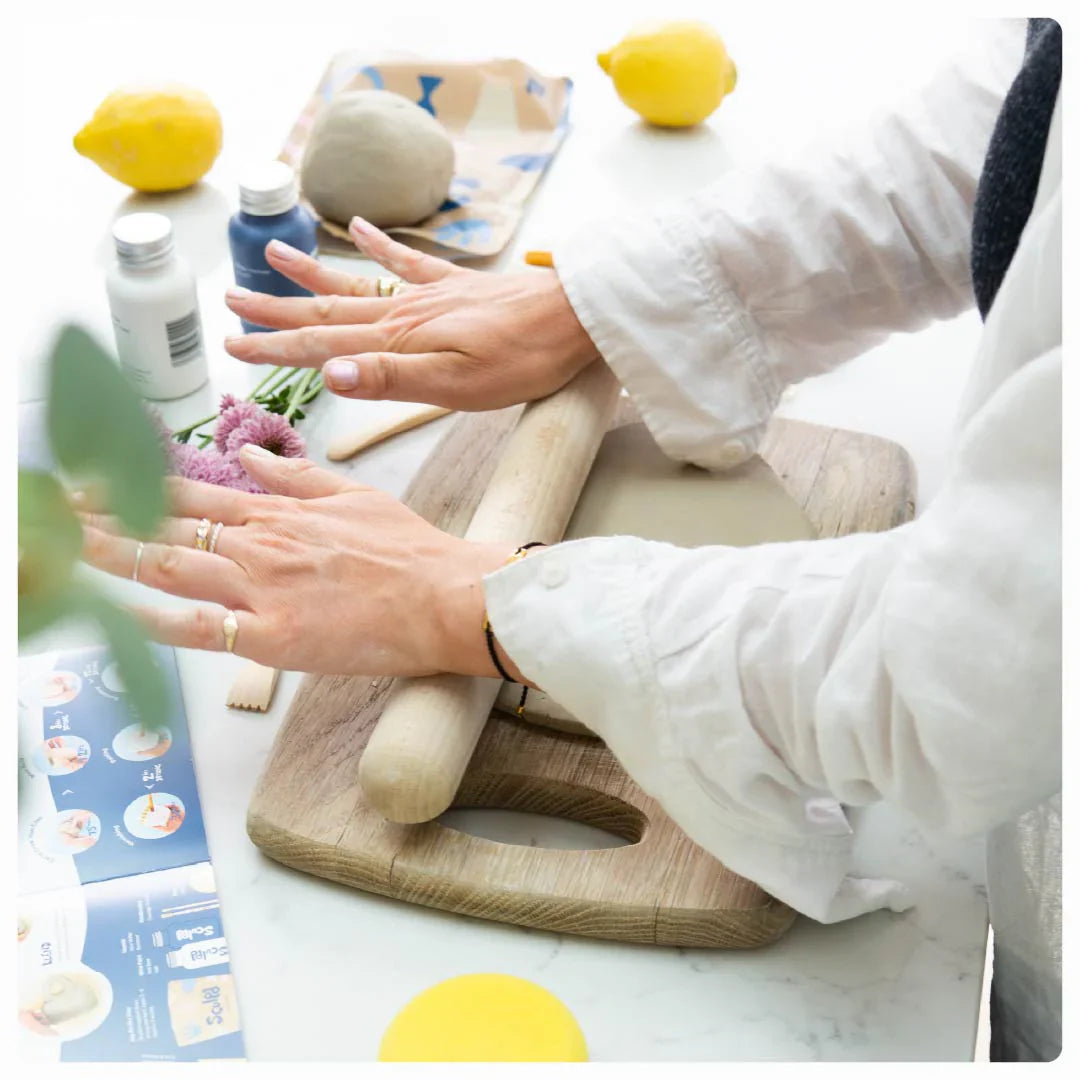 Hands rolling clay and demonstrating pottery techniques, with Sculpd tools and clay displayed on a table